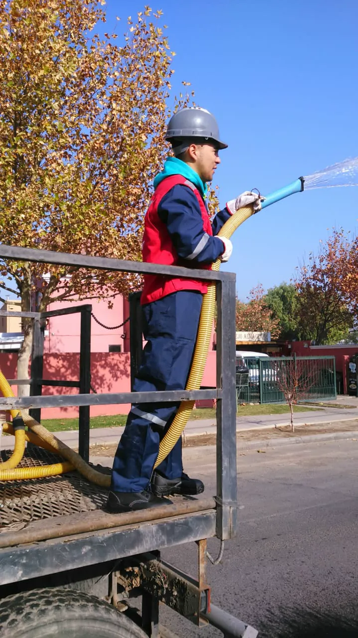 Operario de EDT regando áreas verdes con manguera desde un camión aljibe